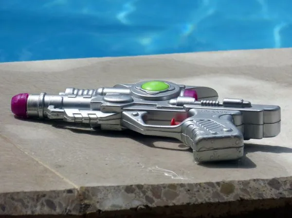 A pump-action water gun resting on the edge of a swimming pool