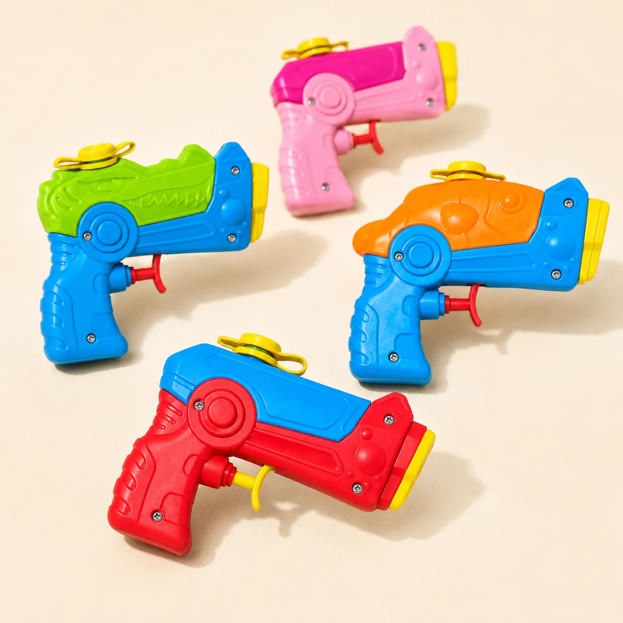 Four small two-colour pocket water pistols on a cream ground