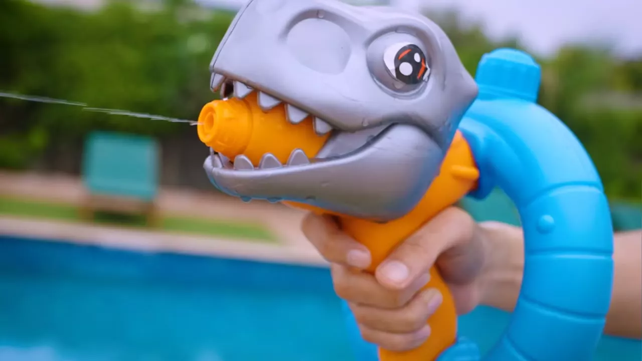 A moulded dinosaur water gun firing beside a pool